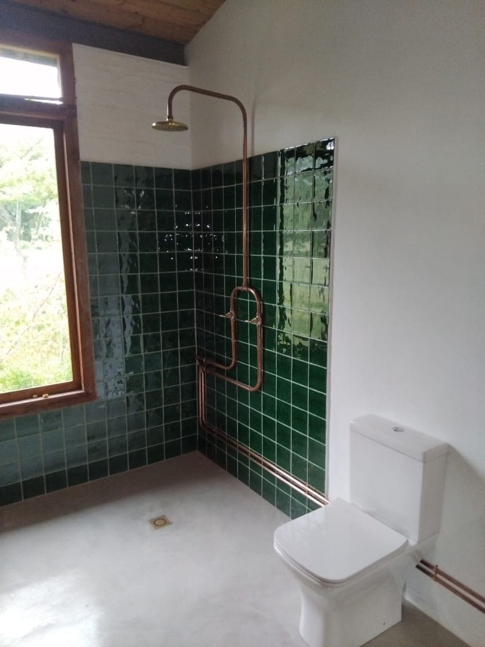 Exposed copper shower pipework on a green-tiled bathroom wall