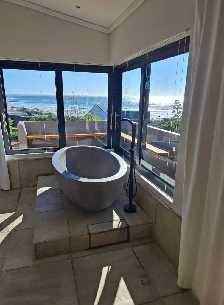 Freestanding stone bath with floor-mounted mixer in front of sea-facing windows